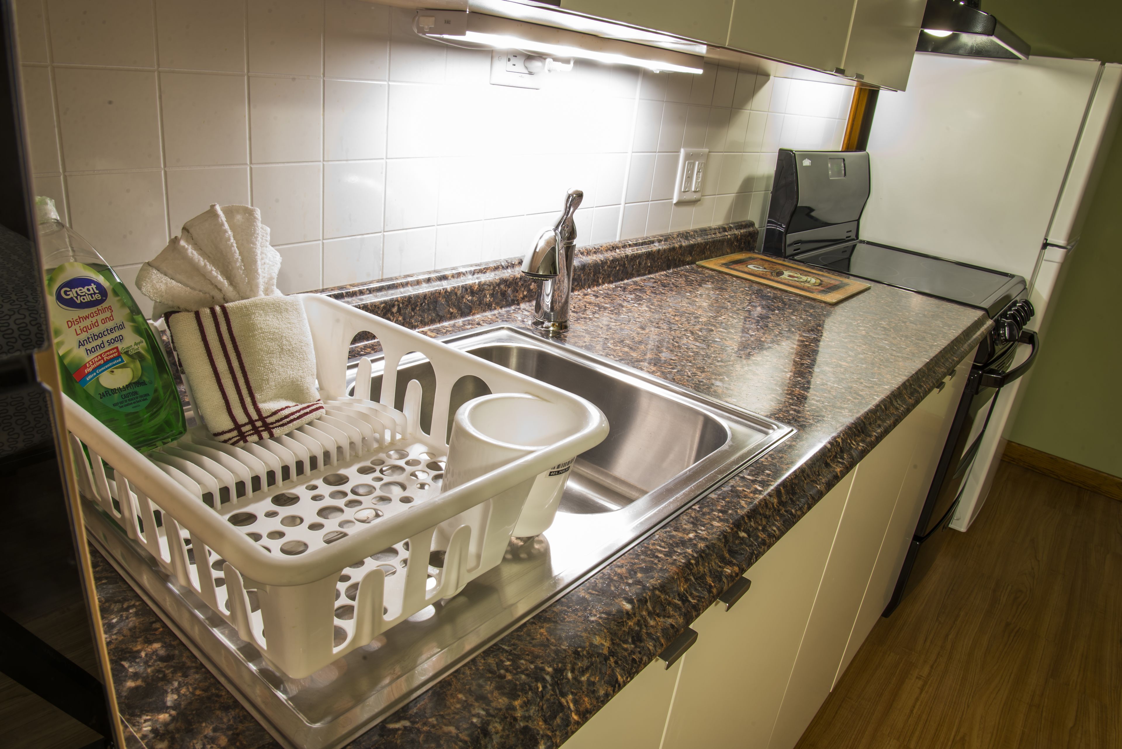 A kitchen with a granite countertop, stainless steel sink, and a dish rack.
