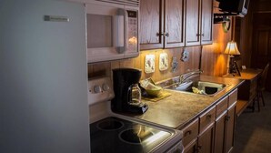 A kitchen with wooden cabinets, a microwave, a coffee maker, and a TV mounted on the wall. - Fairway Overnight & Extended Stay (Manchester)
