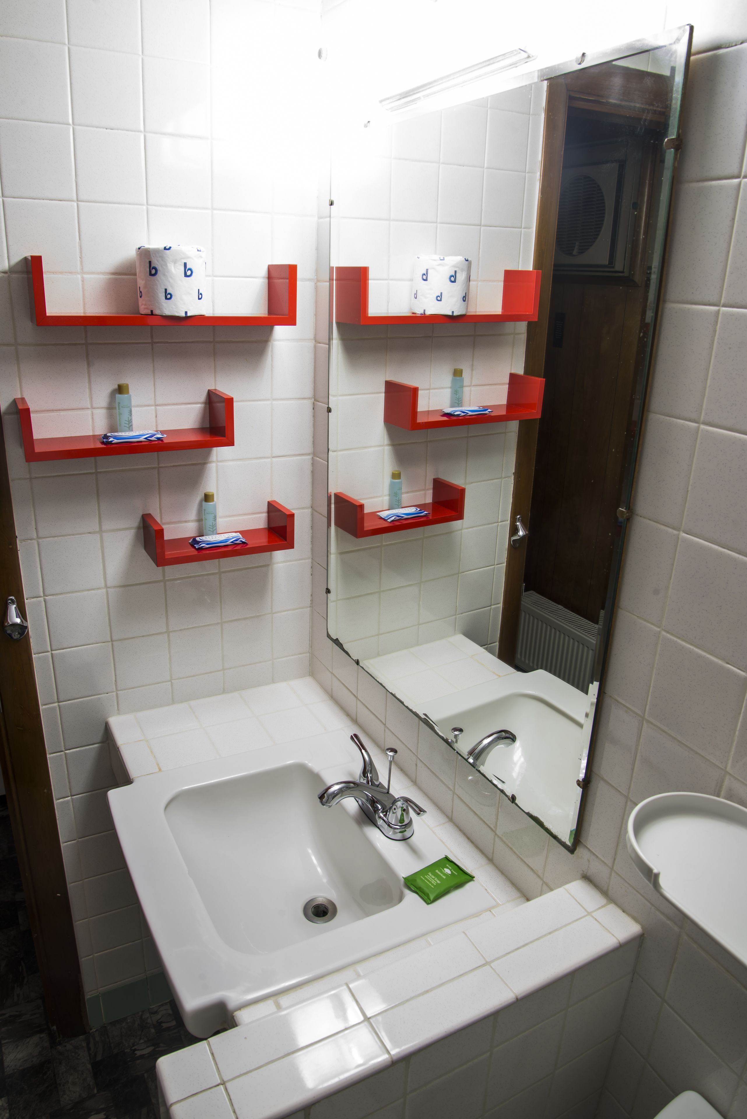 A bathroom with two sinks, red shelves with toiletries, and a large mirror.