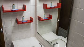 A bathroom with two sinks, red shelves with toiletries, and a large mirror.