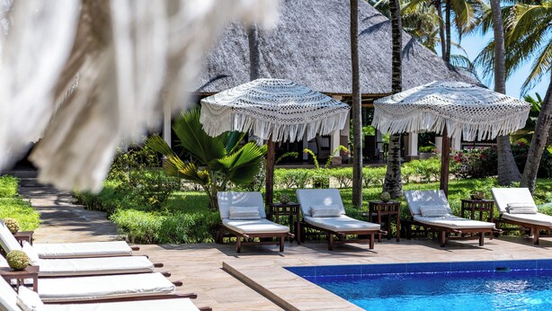 A poolside area with lounge chairs, a pool, and thatched umbrellas. - The Palms Zanzibar - All Inclusive (Dongwe)