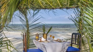 A beach table set with a white tablecloth, two chairs, and a view of the ocean. - The Palms Zanzibar - All Inclusive (Dongwe)