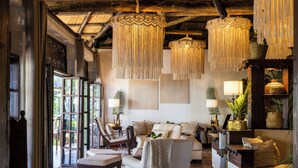 A cozy living room with a sofa, armchairs, and a coffee table. There are hanging lamps, a fireplace, and a bookshelf with decorative items. - The Palms Zanzibar - All Inclusive (Dongwe)