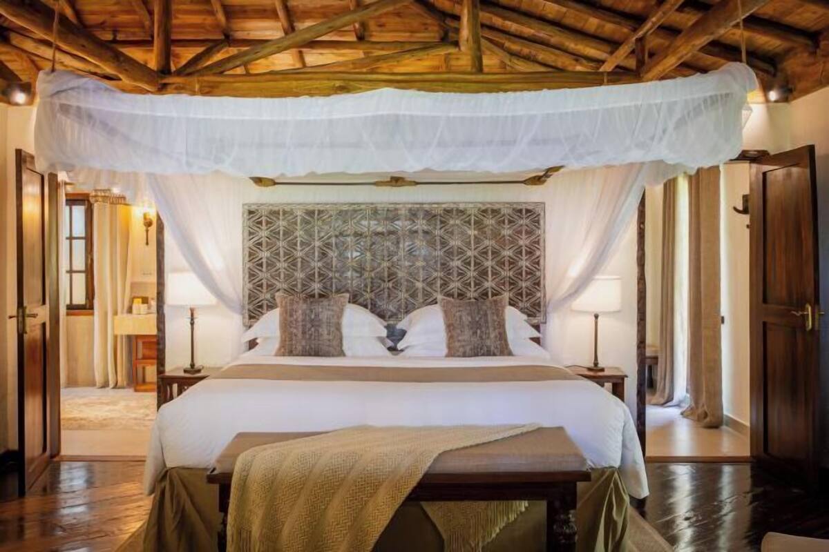 A bedroom with a canopy bed, a geometric headboard, bedside lamps, and a wooden floor.