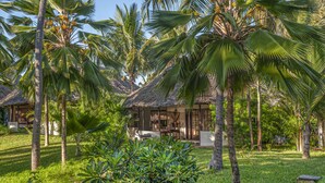 A tropical resort with palm trees, a thatched-roof building, and a well-maintained lawn. - The Palms Zanzibar - All Inclusive (Dongwe)