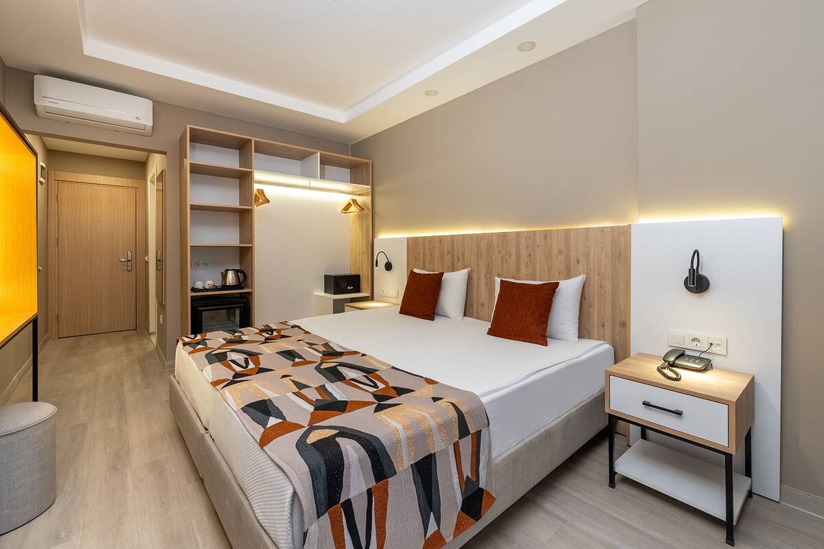 A modern hotel room with a large bed, bedside tables, a wardrobe, and built-in shelves.