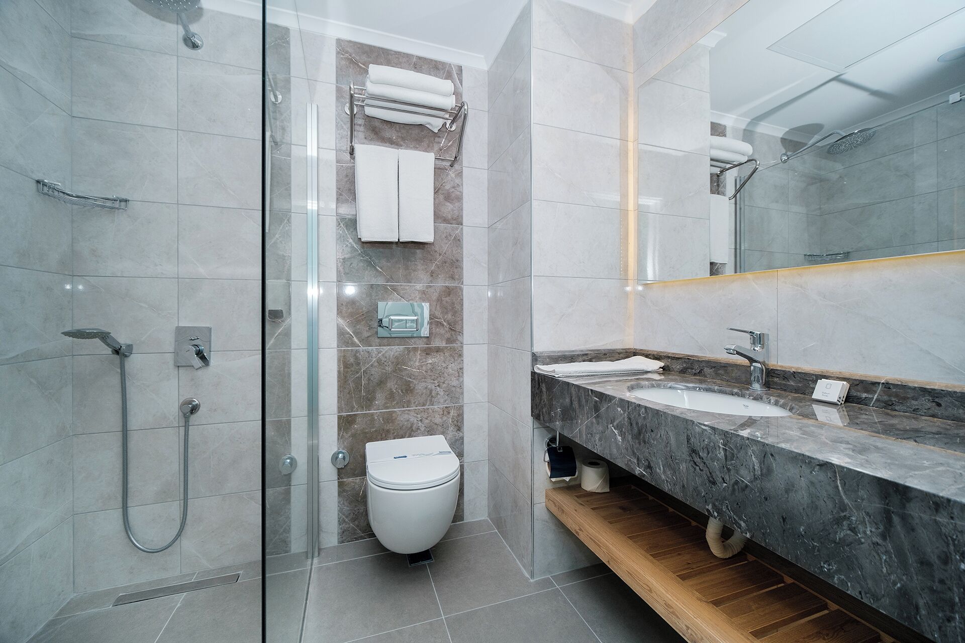 Un baño moderno con cabina de ducha de vidrio, inodoro y tocador con encimera de mármol.