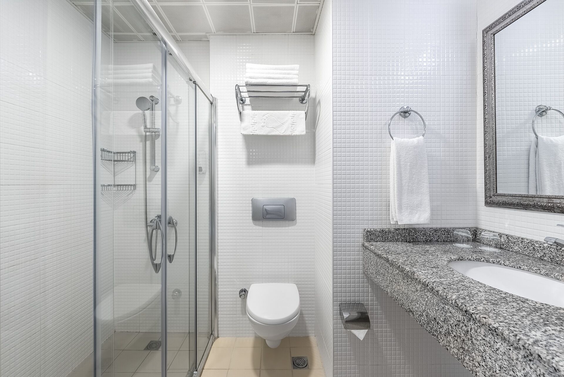 A modern bathroom with a glass-enclosed shower, a white toilet, and a granite countertop sink.