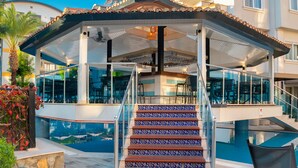 A covered outdoor area with a pool, stairs with patterned tiles, and glass railings. - Villa Sunflower Hotel (Alanya)