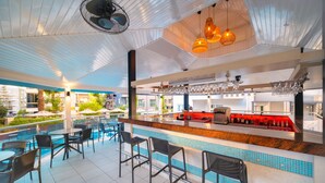 A bar area with a poolside seating arrangement, a bar counter with a red accent, and hanging light fixtures. - Villa Sunflower Hotel (Alanya)
