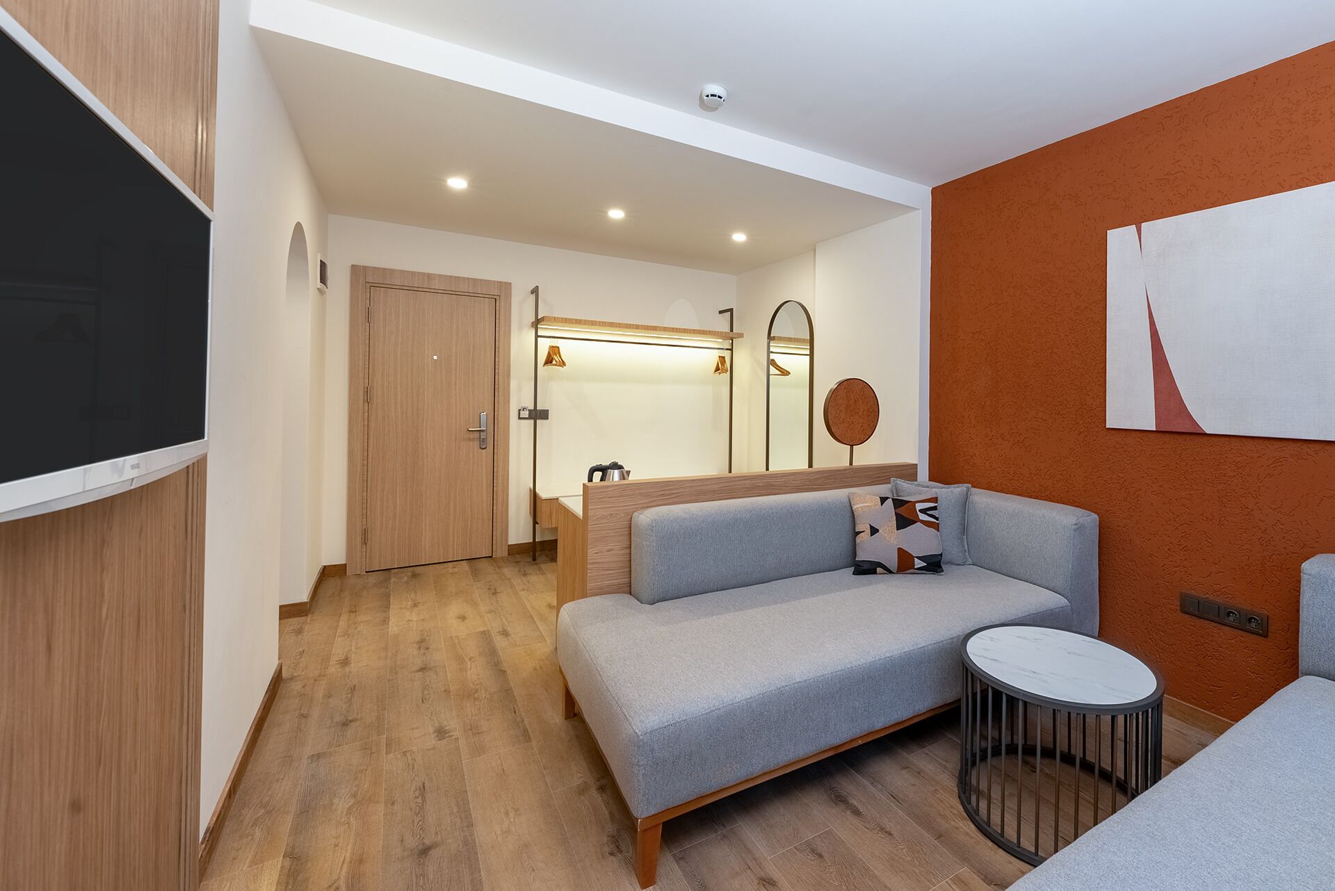 Un soggiorno moderno con un divano grigio, un tavolino rotondo e una TV a parete.