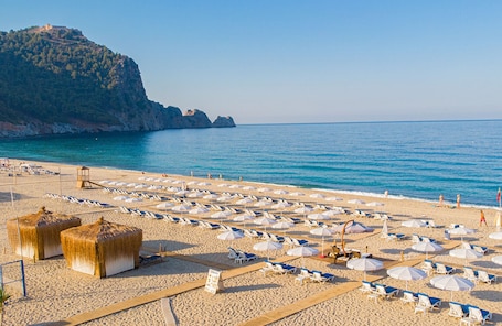A beach with rows of sun loungers and umbrellas, a lifeguard tower, and a mountain in the background.