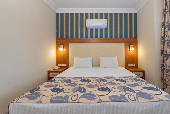 Una habitación de hotel con una cama, dos mesitas de noche, un aire acondicionado de pared y un muro a rayas.