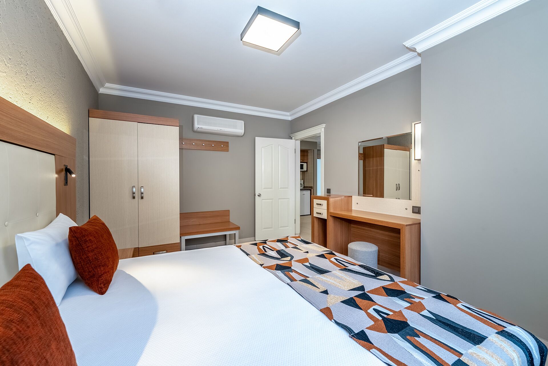 A hotel room with a bed, a desk, a mirror, and a wardrobe.