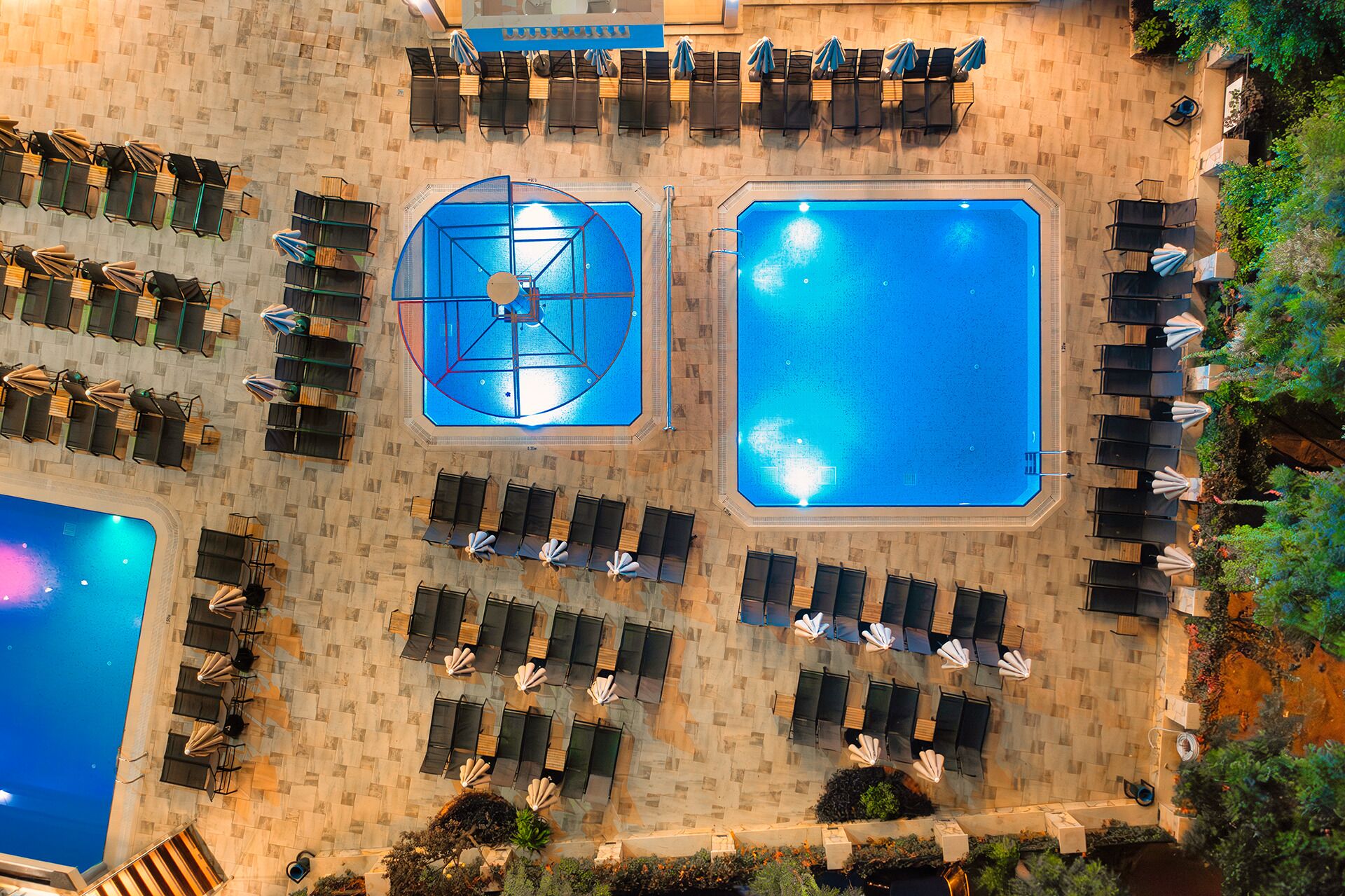 Vue aérienne d’un hôtel doté de deux piscines, de chaises longues et d’un espace détente abrité.