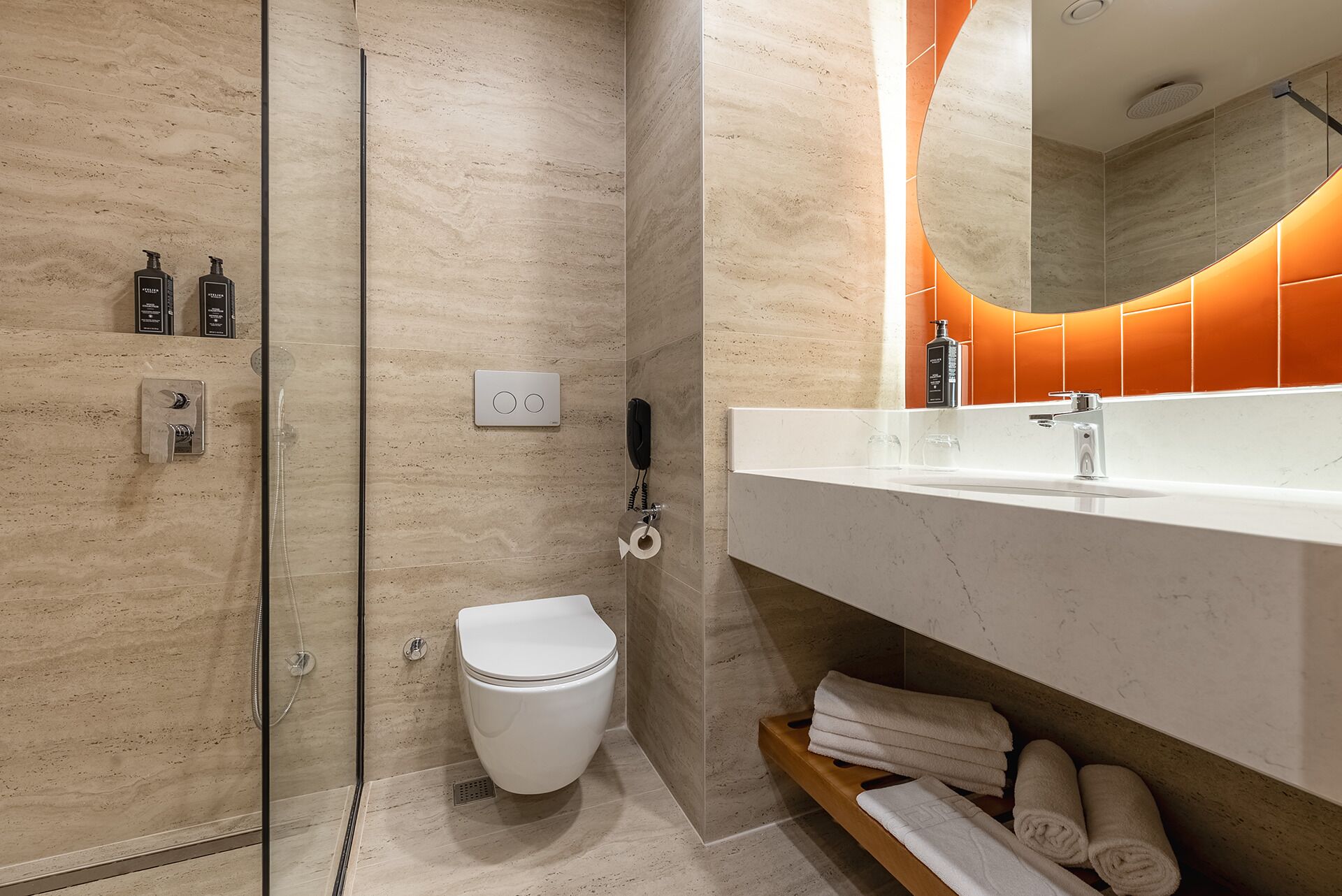 A modern bathroom with a glass shower enclosure, a toilet, a vanity with a mirror, and a shelf with towels.