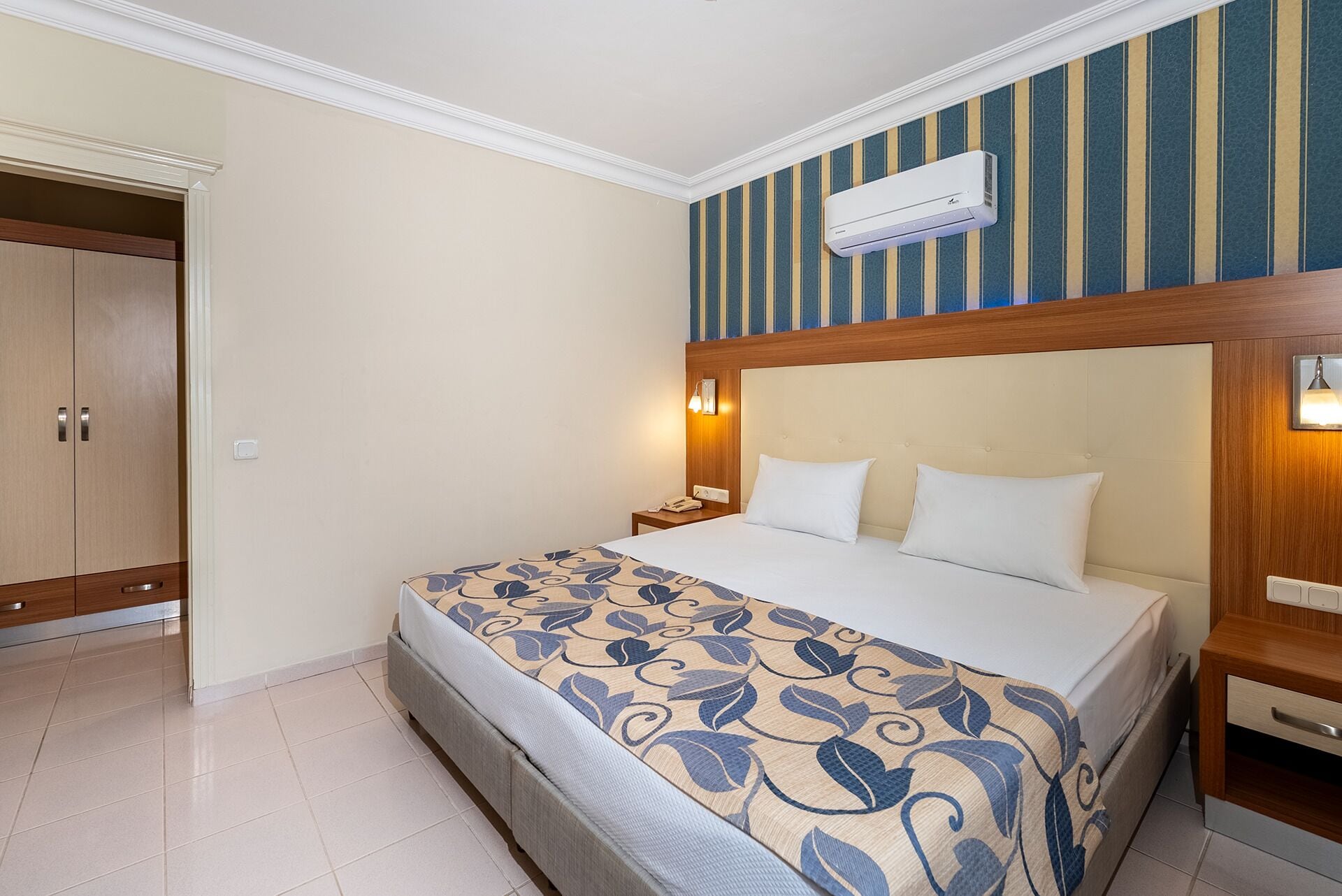 Een hotelkamer met een bed, nachtkastje, lamp en een airconditioning.