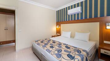 Een hotelkamer met een bed, nachtkastje, lamp en een airconditioning.