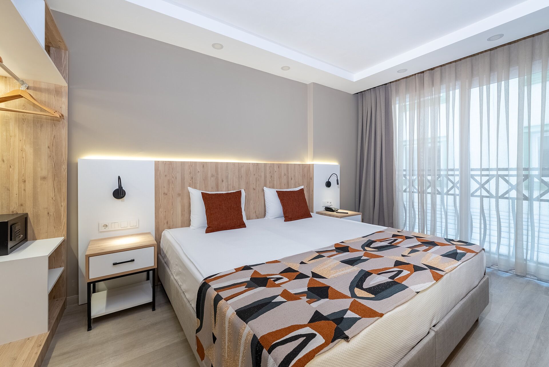 Ein modernes Hotelzimmer mit einem großen Bett, einem Nachttisch, einem Schreibtisch und Meerblick durch transparente Vorhänge.