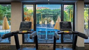 Two exercise bikes with screens, a swimming pool, and outdoor umbrellas in the background. - Villa Sunflower Hotel (Alanya)