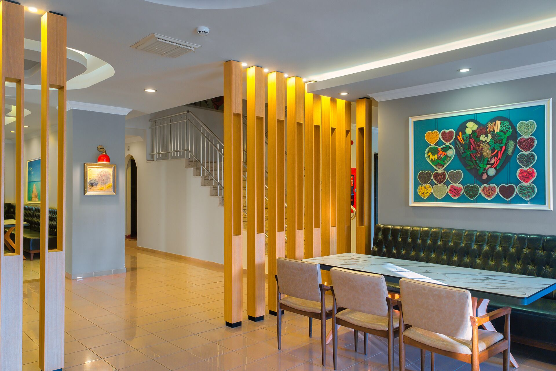 Een modern restaurantinterieur met een houten scheiding, een trap, een eetgedeelte met een tafel en stoelen, en een kleurrijk kunstwerk aan de muur.