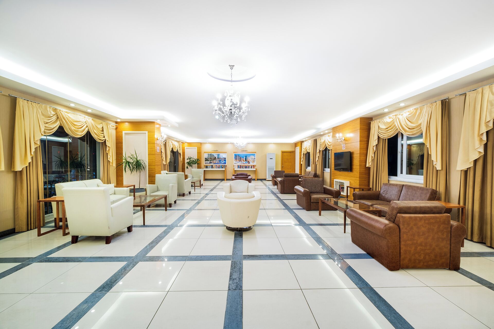 Um hall amplo com área de estar central, um candelabro e uma televisão na parede.