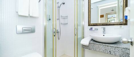 Ein modernes Badezimmer mit einer Duschkabine, einer weißen Toilette, einem Waschbecken mit Granitplatte und einem großen Spiegel mit aufwendigem Rahmen.