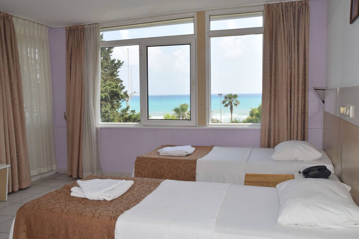 A hotel room with two beds, a window with a view of the sea, and a telephone on the nightstand.