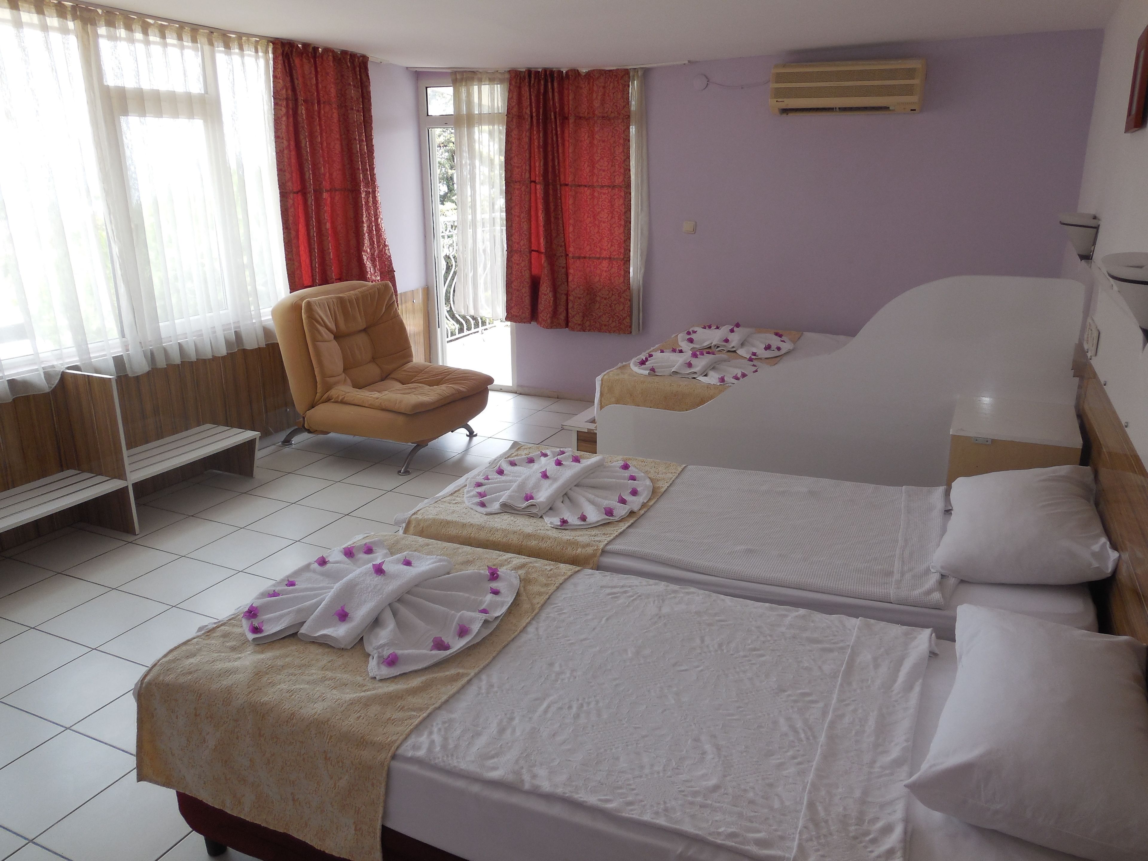 Una habitación de hotel con dos camas, una silla, un banco y una ventana con cortinas.