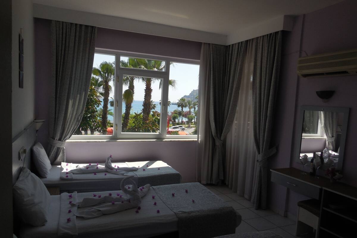 A hotel room with two beds, a large window with curtains, a desk, and a mirror.