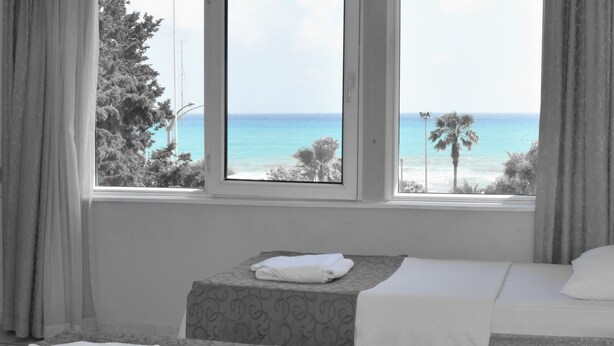 A hotel room with two beds, a window with a view of the ocean, and a neatly folded towel on one bed. - Resitalya Hotel (Alanya)