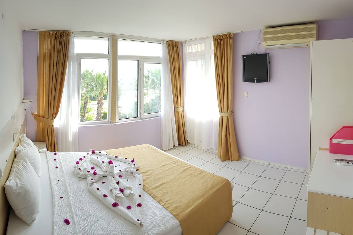 A hotel room with a bed, a TV, an air conditioner, and a window with curtains.