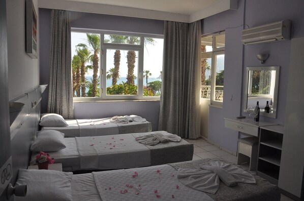A hotel room with two beds, a vanity with a mirror, and a large window with a view of palm trees and the sea. - Resitalya Hotel (Alanya)