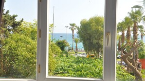 A view through a window of a coastal area with parked cars, palm trees, and a clear sky. - Resitalya Hotel (Alanya)