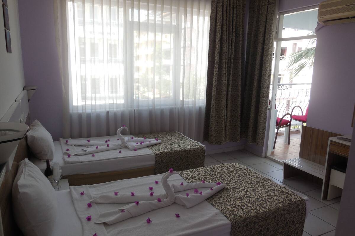 A hotel room with two beds, a balcony with a chair, and a window with sheer curtains.