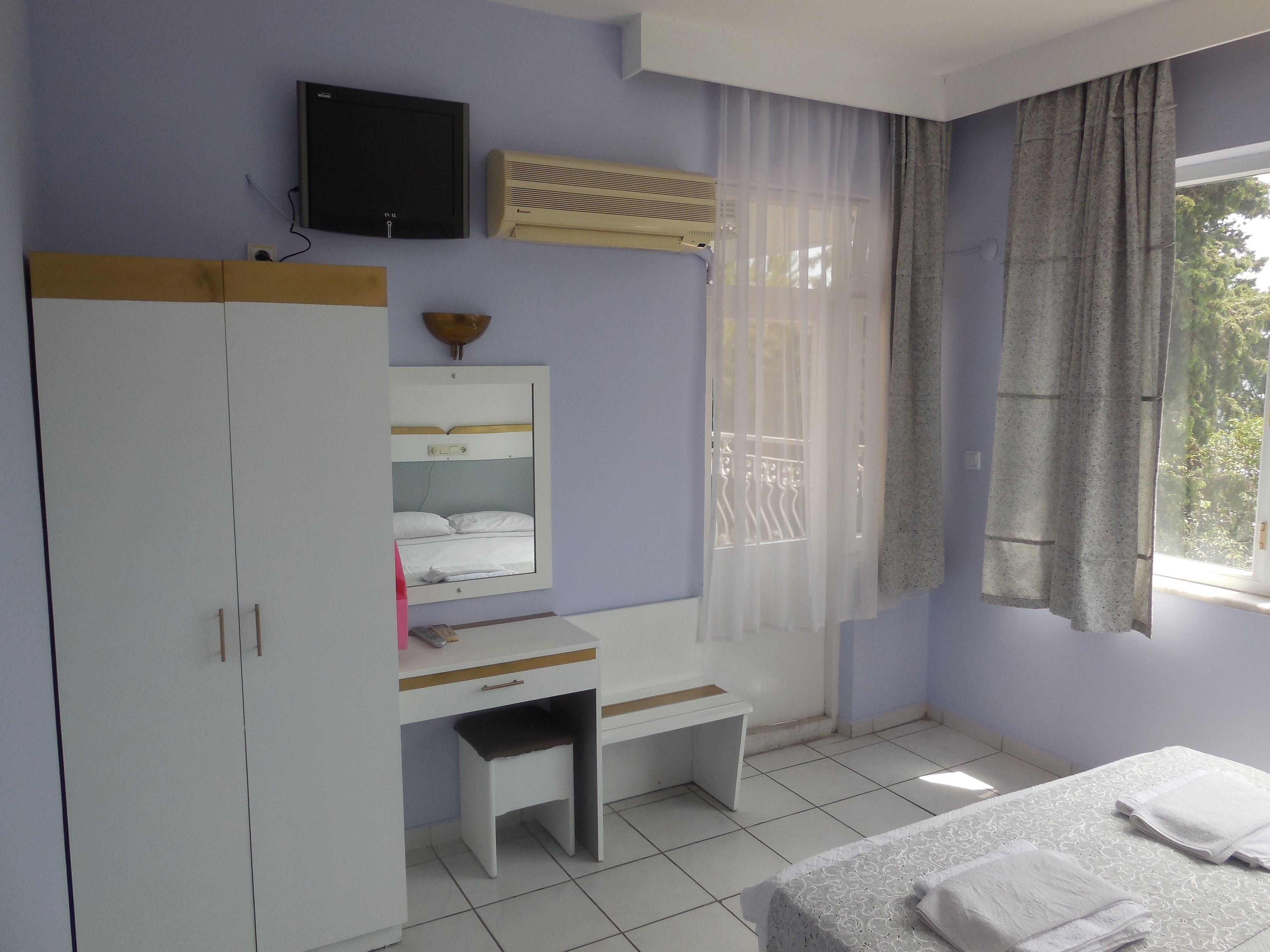 Un dormitorio con cama, escritorio, armario, televisor y ventana con cortinas.