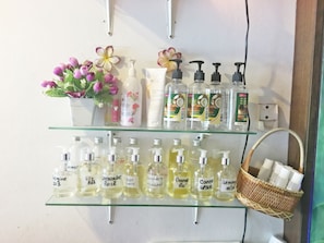 A shelf with various toiletries including bottles of lotion and essential oils, a small potted plant with flowers, and a basket with rolled towels.