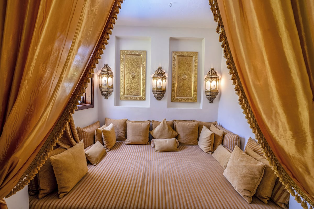 A room with a bed, curtains, wall-mounted lights, and a patterned bedspread.
