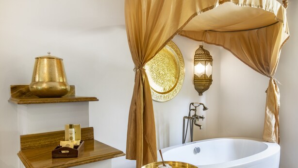 A bathroom with a freestanding bathtub, a vanity with a mirror, and a shelf with a decorative item.