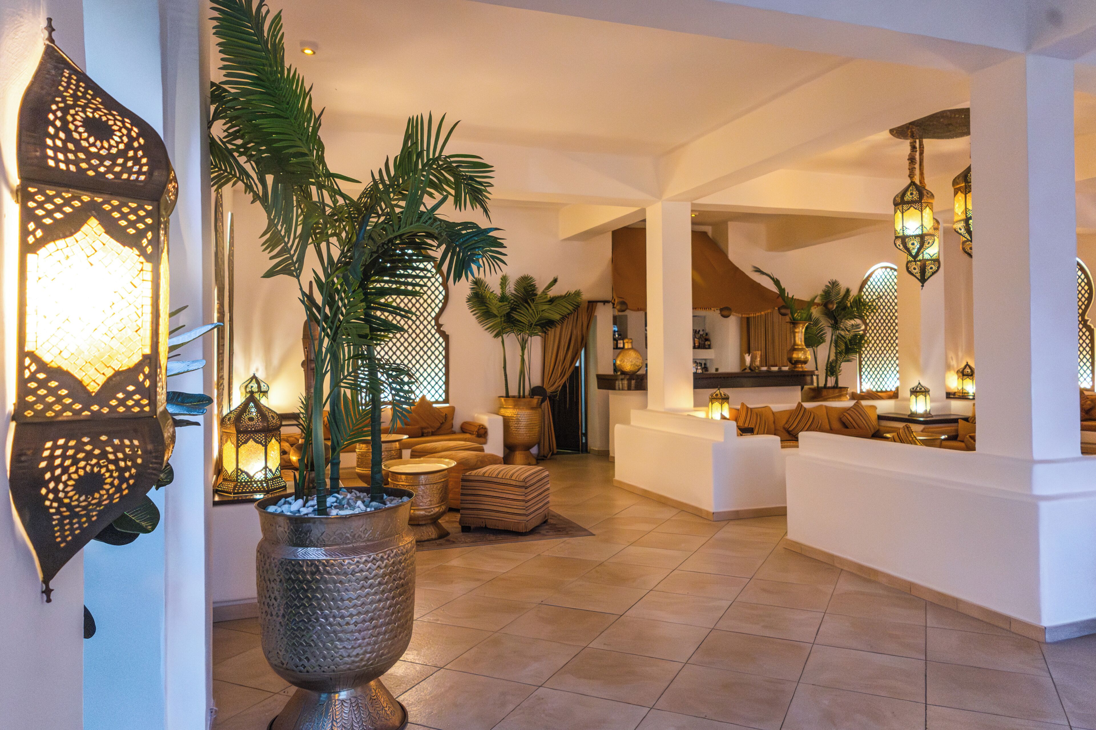 A spacious living area with a large potted plant, a sofa set, and decorative lighting fixtures.