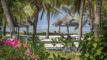 Relax by the ocean with a shaded retreat under thatched umbrellas, surrounded by palm trees and vibrant flowers.