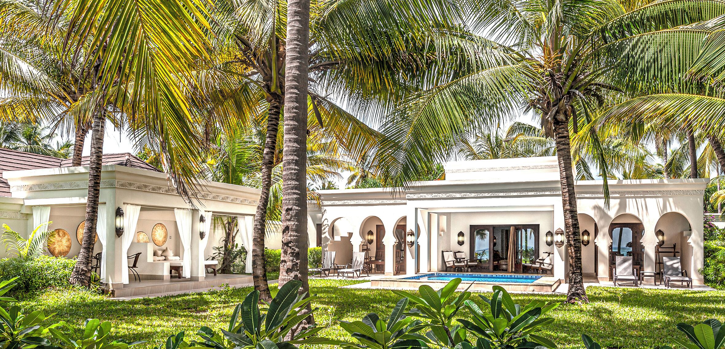 A resort with a pool, palm trees, and a covered patio area.