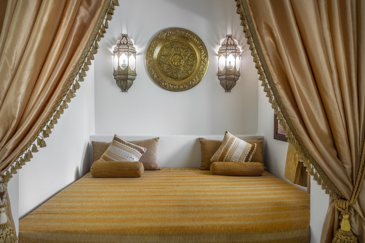 Una cama con ropa de cama a rayas, dos lámparas fijadas a la pared y un plato decorativo encima.