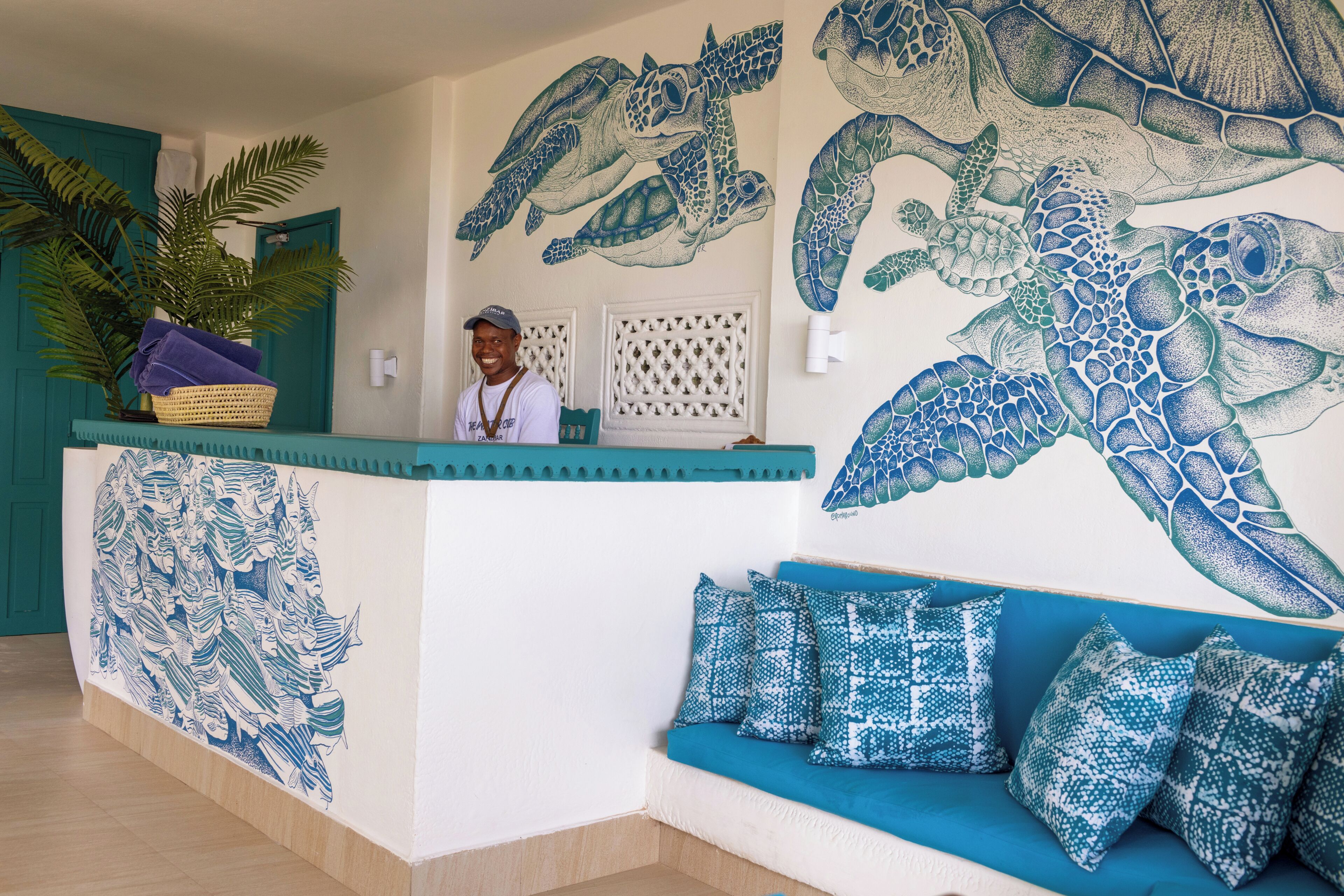 A reception desk with a large turtle mural, a plant, and a seating area with patterned cushions.