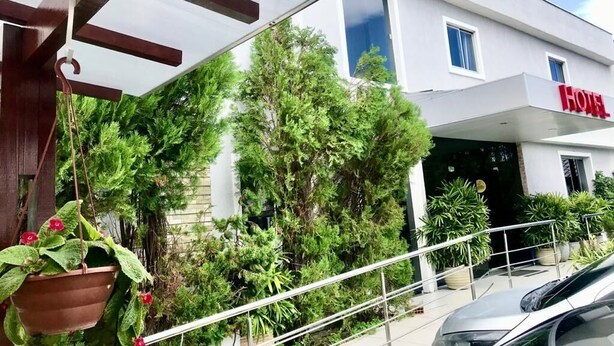 Een hotel ingang met een overdekt terras, plantenbakken en een geparkeerde auto voor.