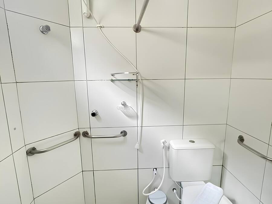 A small, white-tiled bathroom with a toilet, bidet, and shower.