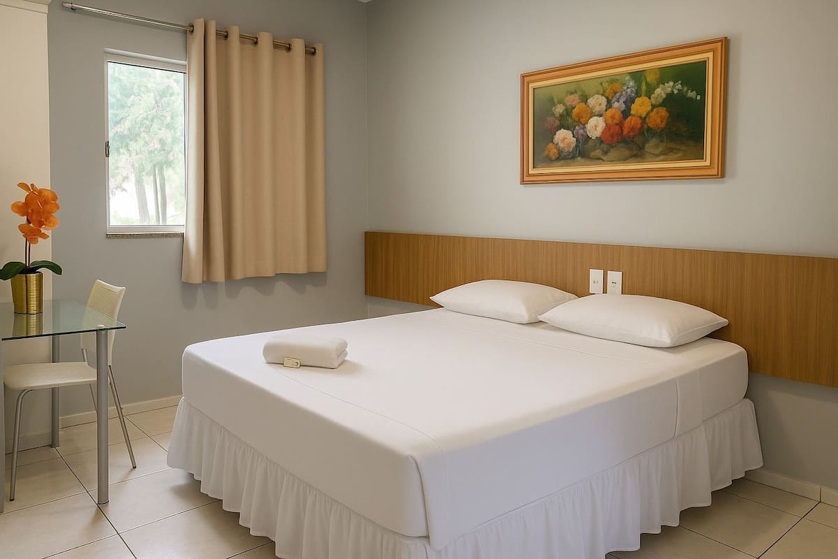 Hotelkamer met een groot bed, nachtkastje, stoel, raam met gordijnen, en een schilderij aan de muur.