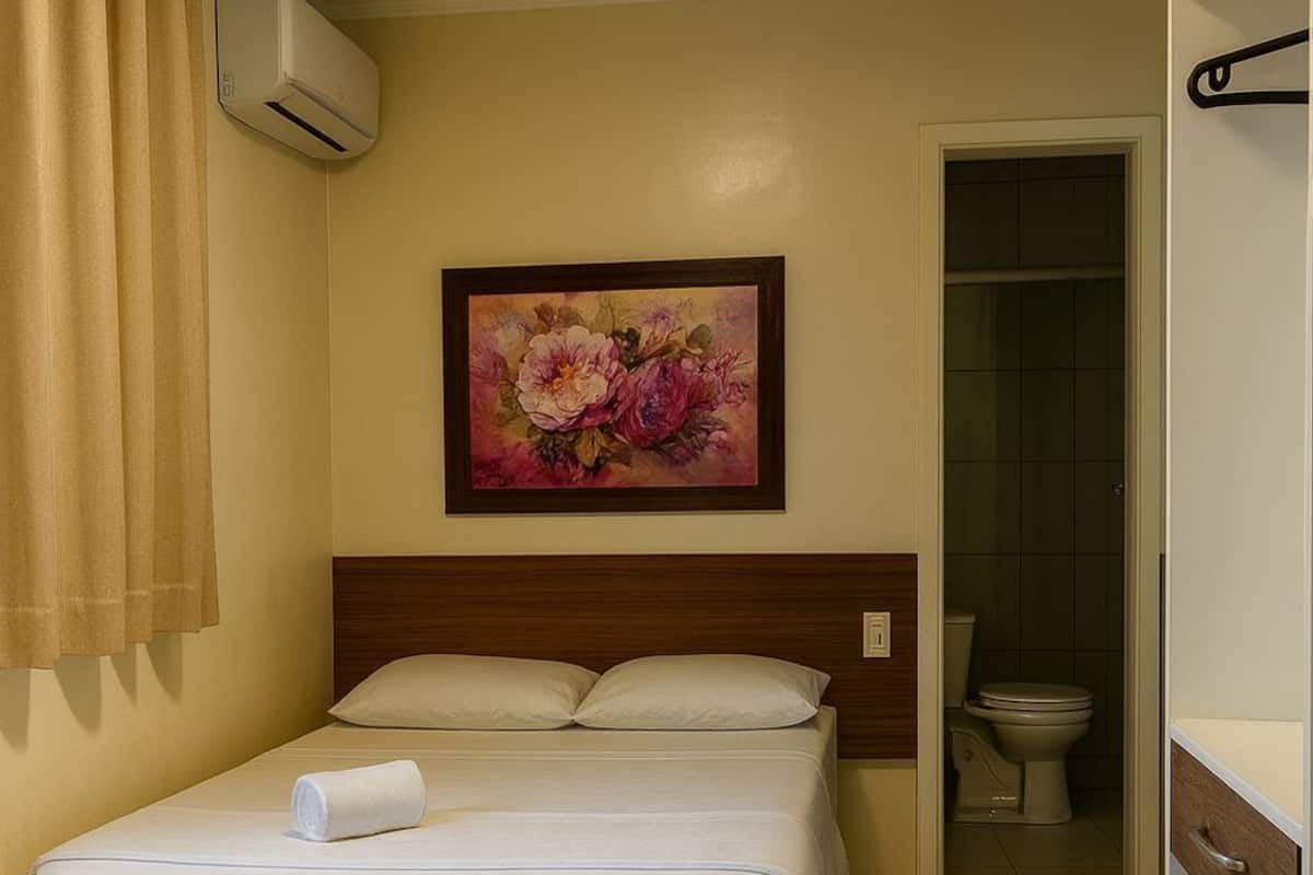 Een hotelkamer met een bed, een schilderij, een badkamer en een klein kastje.