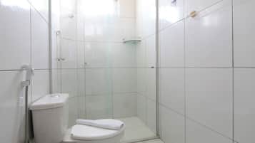 Un baño pequeño y blanco con inodoro, cabina de ducha de vidrio y paredes de azulejos blancos.