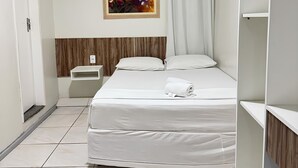 Een hotelkamer met een bed, nachtkastje, airconditioner, schilderij en gordijn.